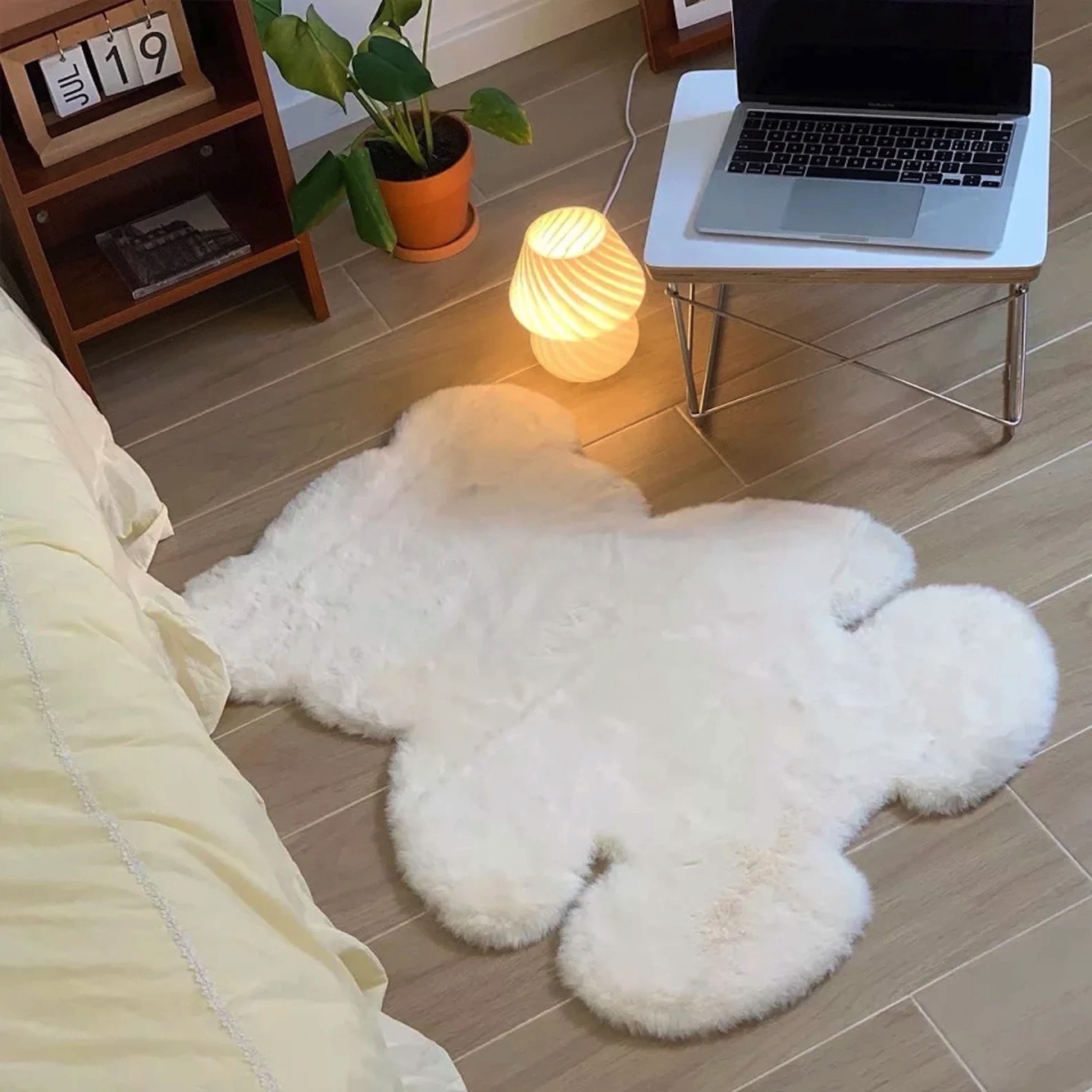 Tapete branco em forma de urso no chão junto a uma cama, mesa com laptop e luminária. 