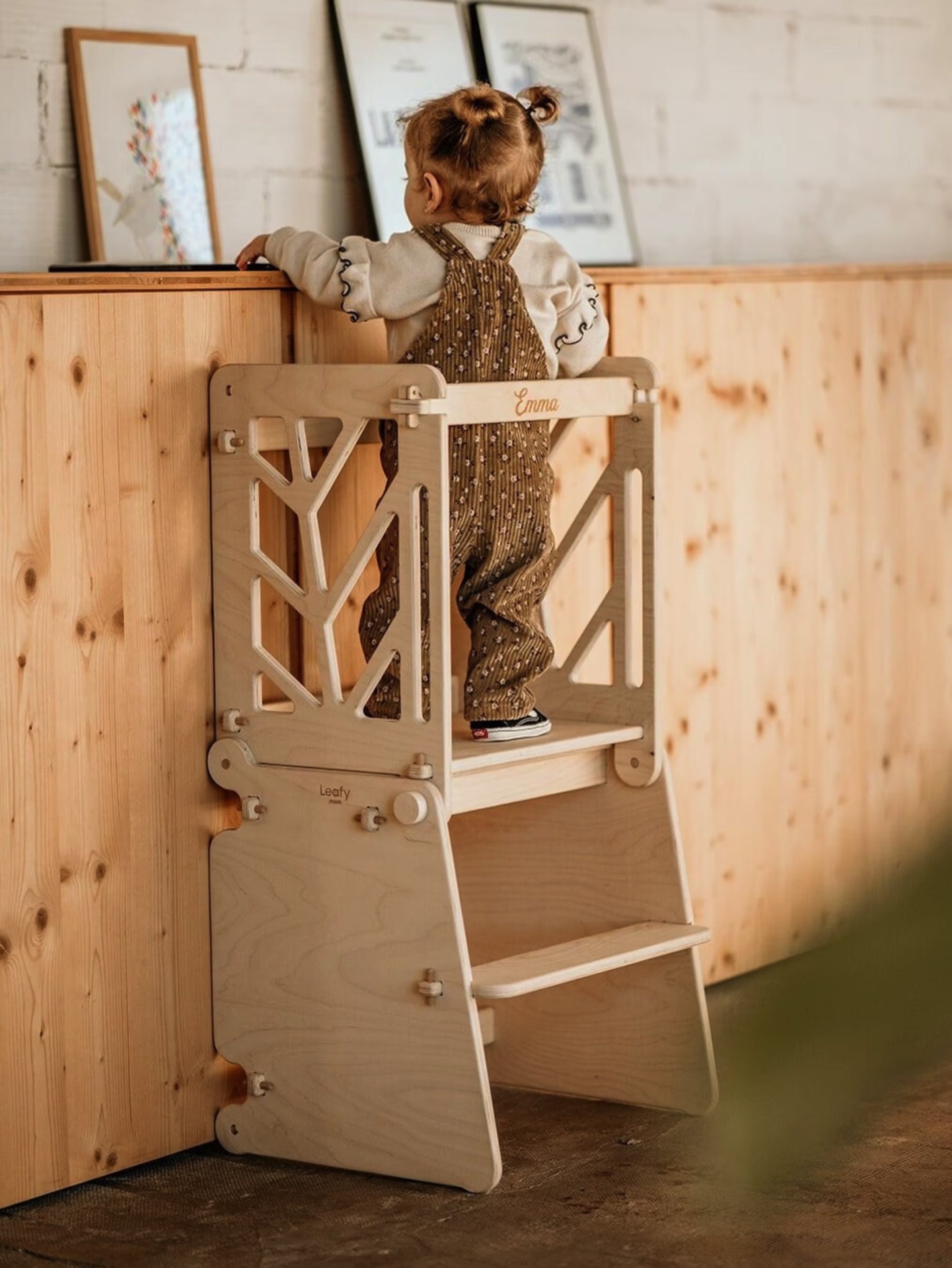 Torre de aprendizagem infantil em madeira clara junto a balcão de madeira com quadros decorativos