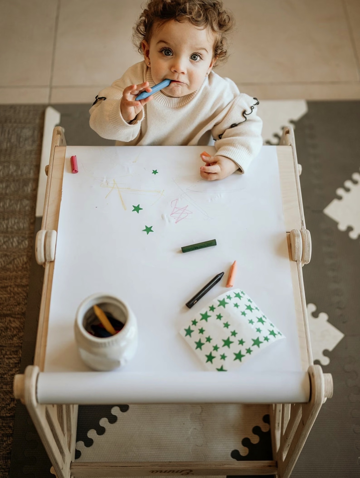 Criança a desenhar numa pequena mesa com lápis de cor e saco estampado de estrelas verdes
