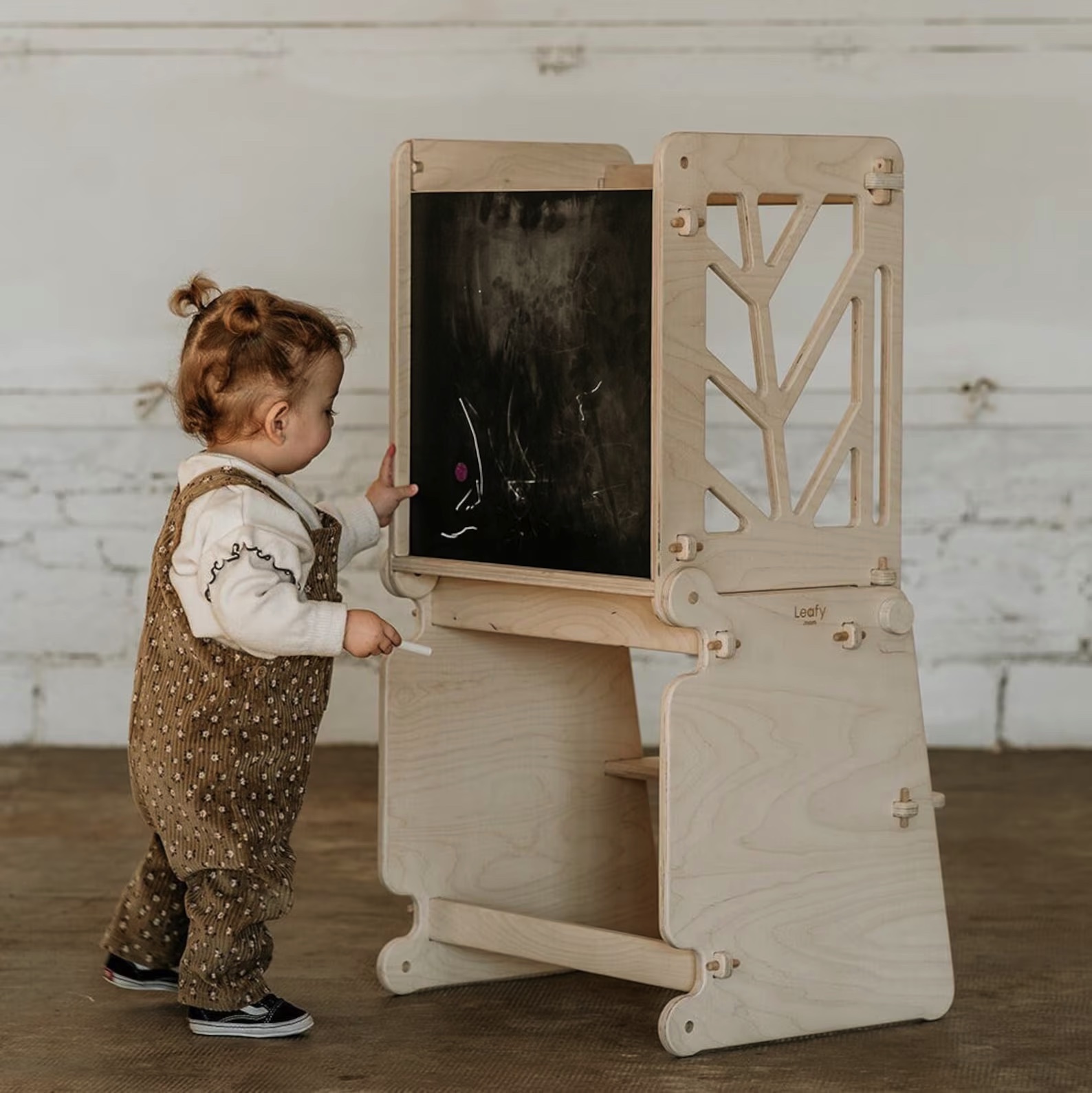 Criança junto a estrutura de madeira com quadro-negro e laterais decorativas