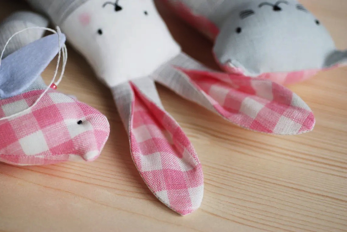 Brinquedos de coelho em tecido rosa e branco e cinza claro em mesa de madeira