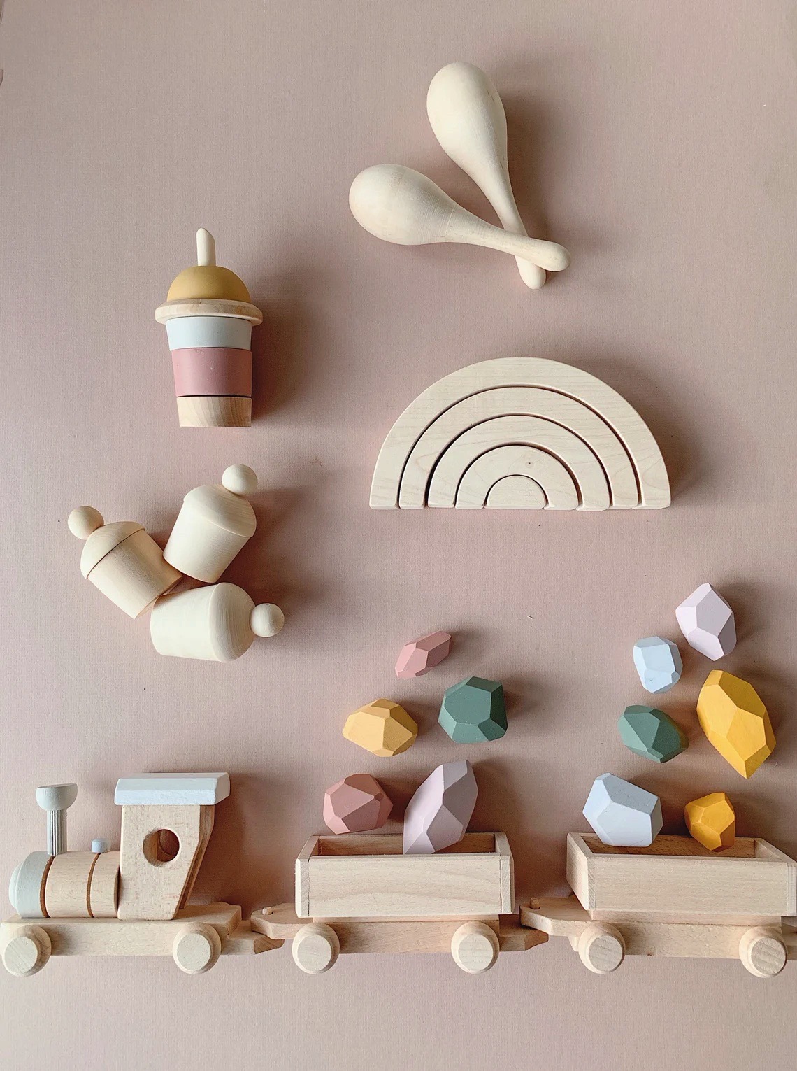 Brinquedos de madeira natural e pintada em cores pastel dispostos sobre fundo rosa