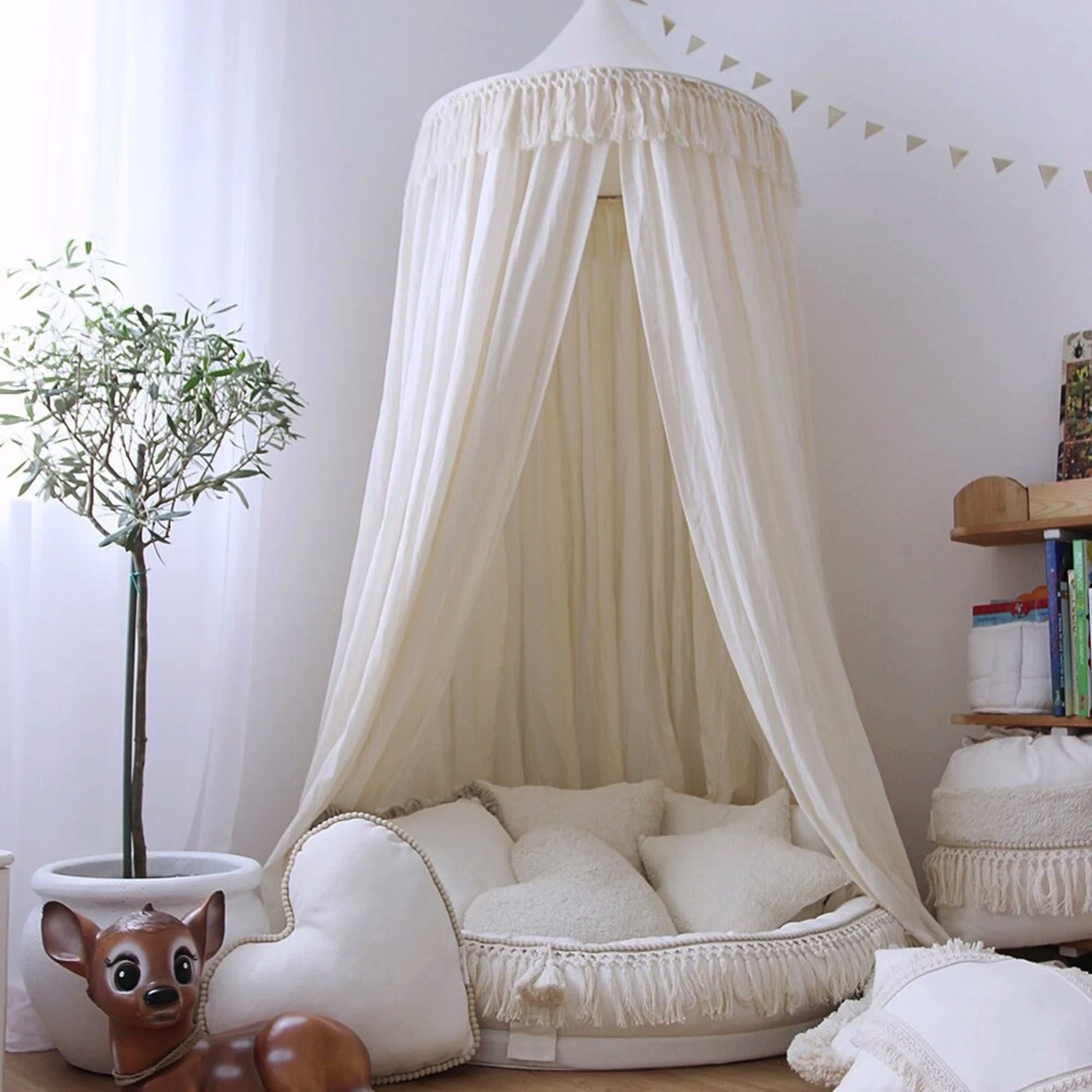 Tenda redonda branca com cortinas e almofadas num quarto com planta e estante