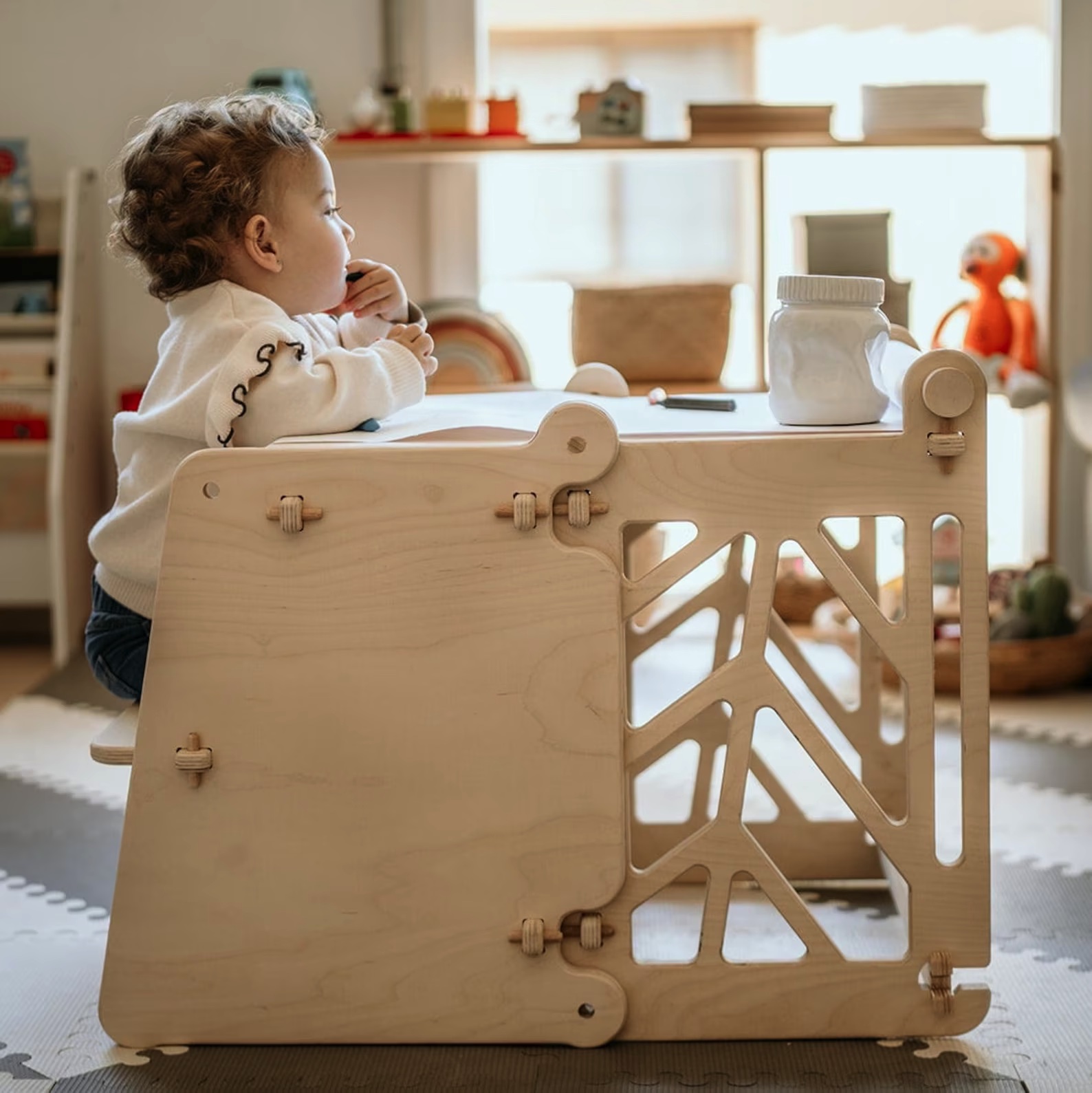 Móvel infantil de madeira clara com design recortado e fechos ajustáveis visto de lado, criança ao lado num espaço interior