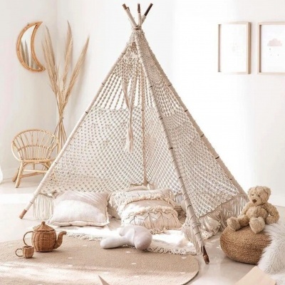 Tenda macramé bege com almofadas, cadeira em vime e ursinho peluche num quarto infantil