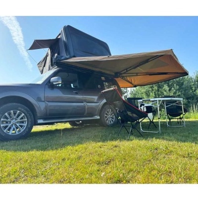 SUV cinza com tenda de campismo lateral, duas cadeiras e mesa em relvado verde