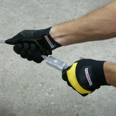 Luvas de proteção preto e amarelo segurando cabo metálico em chão de cimento