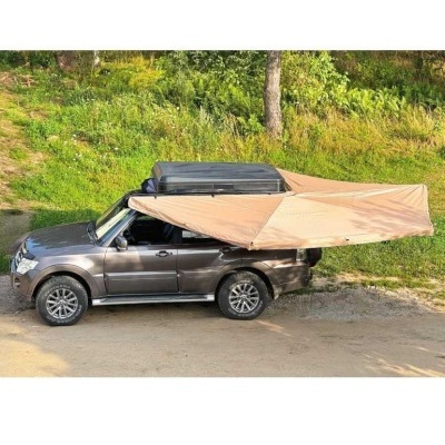 Carro cinzento com tenda bege instalada na porta lateral junto a área verde