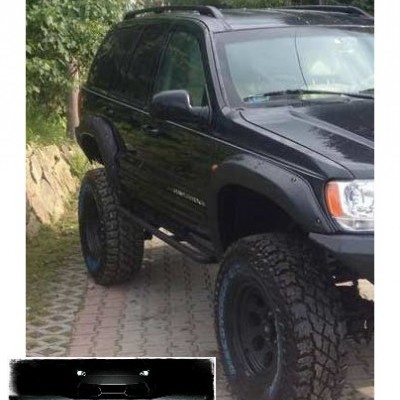 SUV preto com pneus grandes estacionado junto a vegetação