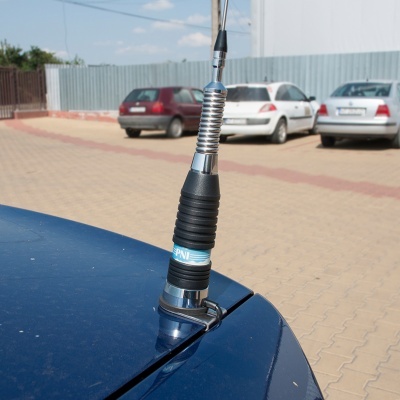 Antena preta e azul para carro montada no tejadilho de um carro azul num parque de estacionamento