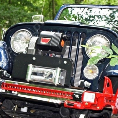 Veículo todo-o-terreno azul escuro com pára-choques e guincho vermelhos e vegetação ao fundo