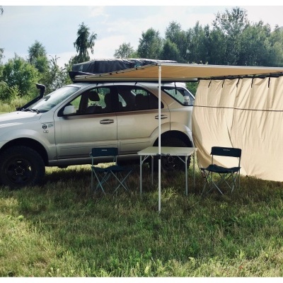 SUV cinzento com toldo bege, duas cadeiras e mesa dobrável num campo verde