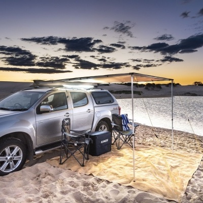 Camião pick-up prateado com toldo e cadeiras numa praia ao pôr do sol