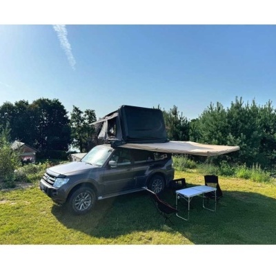 SUV cinzento com tenda e toldo, mesa branca e cadeiras negras num campo