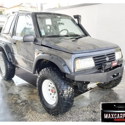 Veículo Suzuki Samurai todo-o-terreno cinzento com pneus grandes e reforços, estacionado em espaço aberto