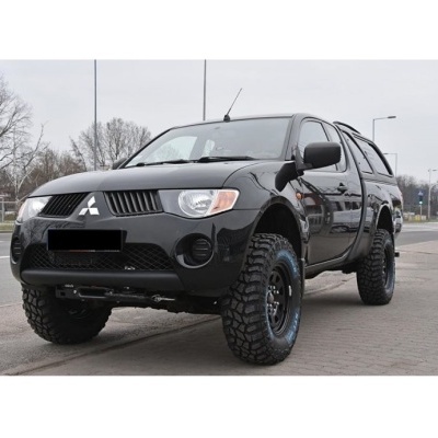 Pick-up Mitsubishi preto com capota e pneus grandes estacionada na estrada
