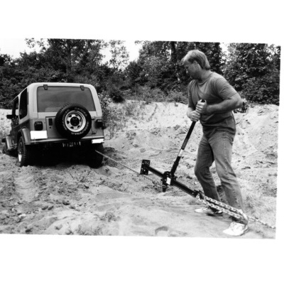 Homem a usar alavanca para soltar carro preso na areia, com vegetação ao fundo