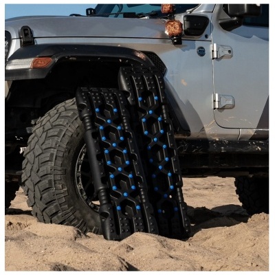 Tanques de recuperação pretos com pinos azuis ao lado da roda de um jipe cinzento na areia
