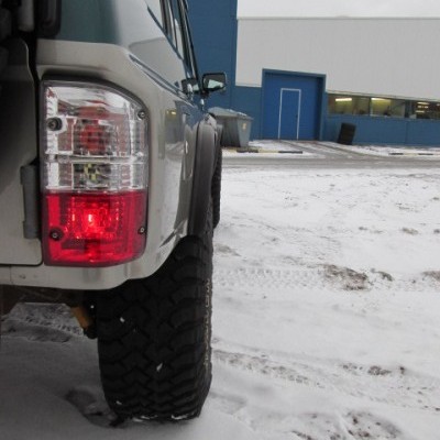 Traseira de veículo todo-o-terreno cinza em chão com neve e edifício azul ao fundo