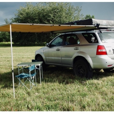 Carro 4x4 prata com toldo amarelo e mesa com cadeiras azuis em campo