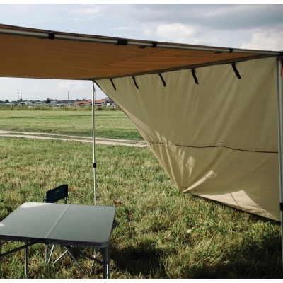 Toldo de campismo bege montado num campo verde com mesa e cadeiras dobráveis ao lado.