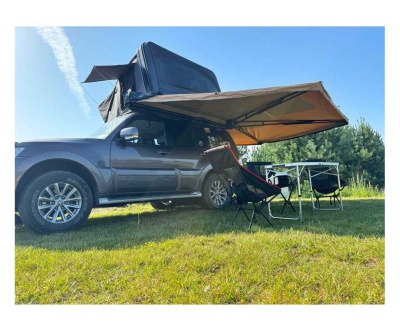 SUV cinza com tenda de campismo lateral, duas cadeiras e mesa em relvado verde