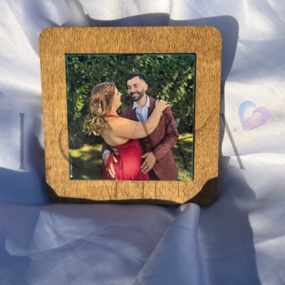 Moldura de madeira com fotografia de casal abraçado ao ar livre sobre tecido branco.