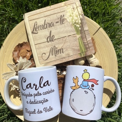 Dois canecas brancas com texto e ilustração, puzzle em madeira com mensagem, tudo sobre prato de madeira sobre relva verde.