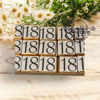 Pacote de chocolates branco com números 81 e 18 e flores ao fundo