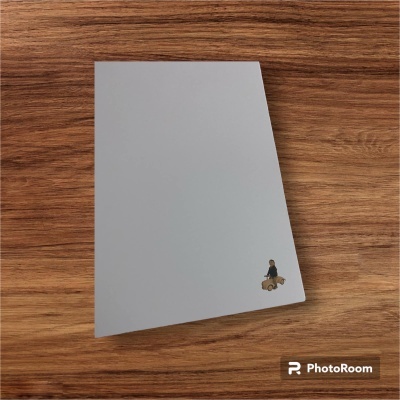 Caderno com capa branca e pequeno desenho no canto inferior direito sobre superfície de madeira