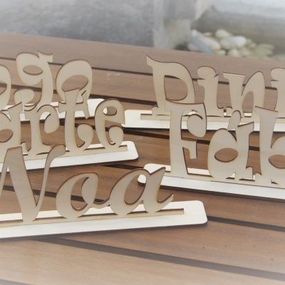 Placas de nomes em madeira clara recortada num suporte horizontal em mesa de madeira