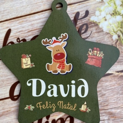 Estrela de madeira verde com rena e texto 'David Feliz Natal', sobre madeira clara com flores brancas