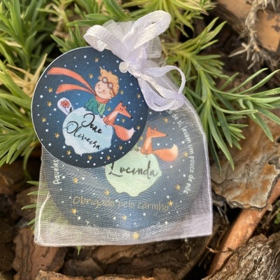 Bolsa de organza branca com etiqueta do Príncipezinho sobre casca de árvore e plantas