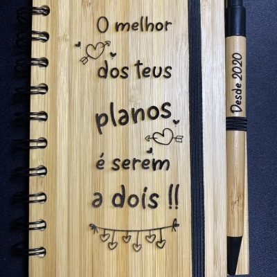 Caderno e caneta em madeira clara com texto gravado e elástico para fechar
