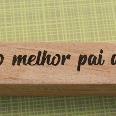 Objeto de madeira clara com gravação 'Para o melhor pai do mundo' sobre superfície verde quadriculada