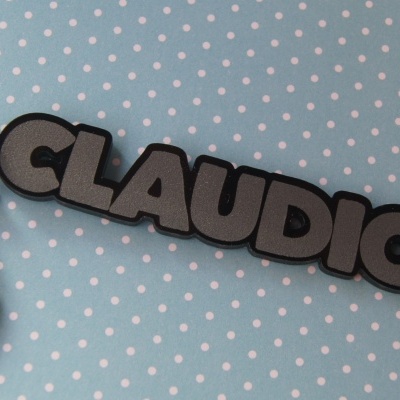 Porta-chaves com o nome CLAUDIO em letras cinzentas sobre fundo azul com pontos brancos