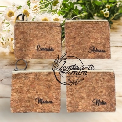 Quatro carteiras de cortiça com nomes gravados em preto e fecho, sobre mesa de madeira com flores ao fundo