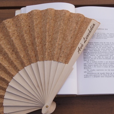 Abanador de madeira e cortiça com texto 'As Leciadas' sobre livro aberto
