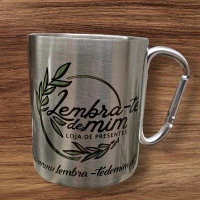 Caneca metálica prateada com texto e folhas verdes sobre superfície de madeira