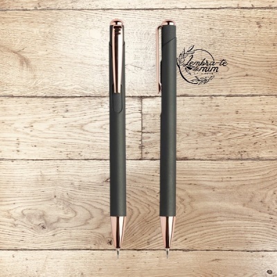 Duas canetas pretas com detalhes dourados rosa em fundo de madeira clara com texto caligráfico