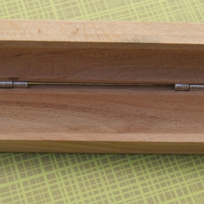 Estojo de madeira retangular aberto com dobradiças metálicas sobre superfície quadriculada