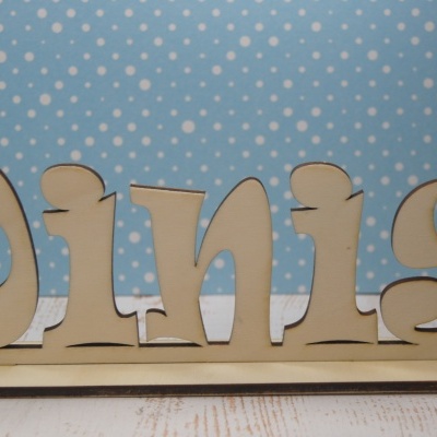 Objeto decorativo de madeira com palavra Dinis, fundo azul com bolinhas brancas