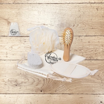 Conjunto de acessórios de banho com escova, esponja, pedra-pomes, luva e saco branco sobre madeira clara