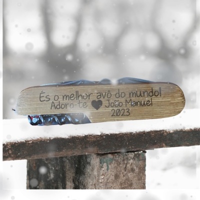 Faca multiusos com cabo em madeira e metal azul escuro gravada com mensagem personalizada, apoiada em superfície com neve