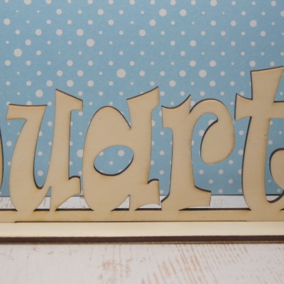 Palavra Duarte em letras de madeira num suporte base sobre fundo azul com bolas brancas