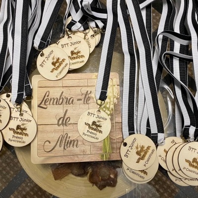 Medalhas de madeira penduradas em fitas listradas e quadro com texto 'Lembra-te de Mim'