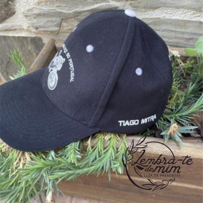 Boné preto com bordados brancos do SL Benfica e nome Tiago Mitra, sobre vegetação e fundo de pedra