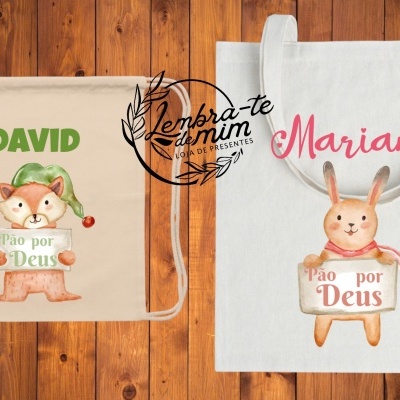 Mochilas de tecido com nomes e ilustrações de animal segurando placas com texto 'Pão por Deus', sobre fundo de madeira.