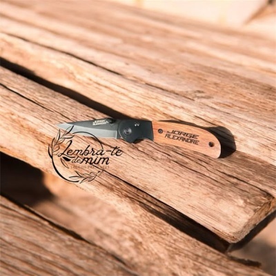 Faca de bolso com lâmina preta e cabo em madeira clara sobre madeira rústica