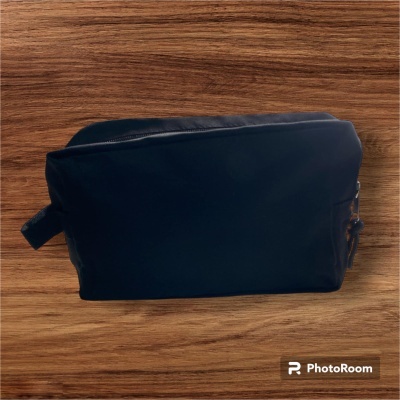 Necessaire preta retangular sobre superfície de madeira clara.